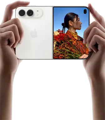 iPhone Duo, finition blanc stellaire, tenu à deux mains en position horizontale, déplié, le volet extérieur gauche présente les caméras arrière Fusion 48 MP, le volet extérieur droit présente l’écran externe affichant une personne qui se fait photographier et peut voir son propre visage pendant la prise de vue à l’aide de Duo Preview