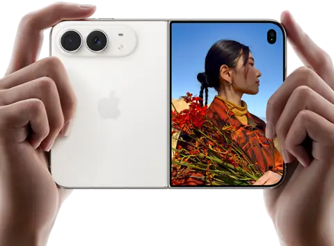 iPhone Duo, finition blanc stellaire, tenu à deux mains en position horizontale, déplié, le volet extérieur gauche présente les caméras arrière Fusion 48 MP, le volet extérieur droit présente l’écran externe affichant une personne qui se fait photographier et peut voir son propre visage pendant la prise de vue à l’aide de Duo Preview