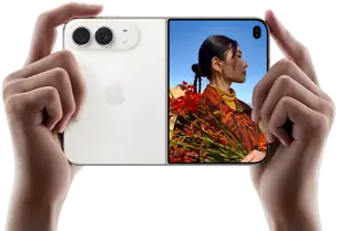 iPhone Duo, finition blanc stellaire, tenu à deux mains en position horizontale, déplié, le volet extérieur gauche présente les caméras arrière Fusion 48 MP, le volet extérieur droit présente l’écran externe affichant une personne qui se fait photographier et peut voir son propre visage pendant la prise de vue à l’aide de Duo Preview