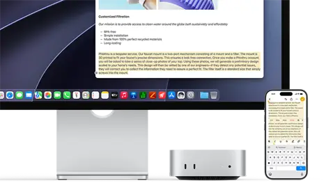 Mac mini de face, glissé sous un Studio Display, un iPhone se trouve à droite de l’appareil et de l’écran, du texte sélectionné avec les commandes Couper, Copier, Coller et Remplissage automatique en haut de l’iPhone correspond au texte surligné à l’écran, illustrant le fonctionnement du presse-papiers universel