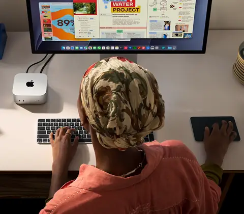 Une personne assise à un bureau utilise un Mac mini connecté à un Studio Display, Magic Keyboard, Magic Trackpad, divers objets