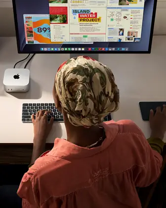 Une personne assise à un bureau utilise un Mac mini connecté à un Studio Display, Magic Keyboard, Magic Trackpad, divers objets