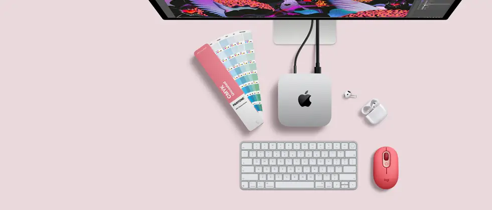 Mac mini, dessus, aluminium argent, angles arrondis, logo Apple noir brillant centré, connecté par un câble, Studio Display partiellement visible en haut, AirPods 4, boîtier ouvert, pastilles de couleur Pantone, et clavier et souris Logitech rouges